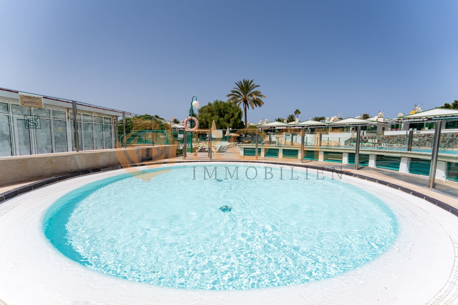 Round-shaped swimming pool with surrounding sun terrace and integrated privacy screen Round-shaped swimming pool with surrounding sun terrace and integrated privacy screen