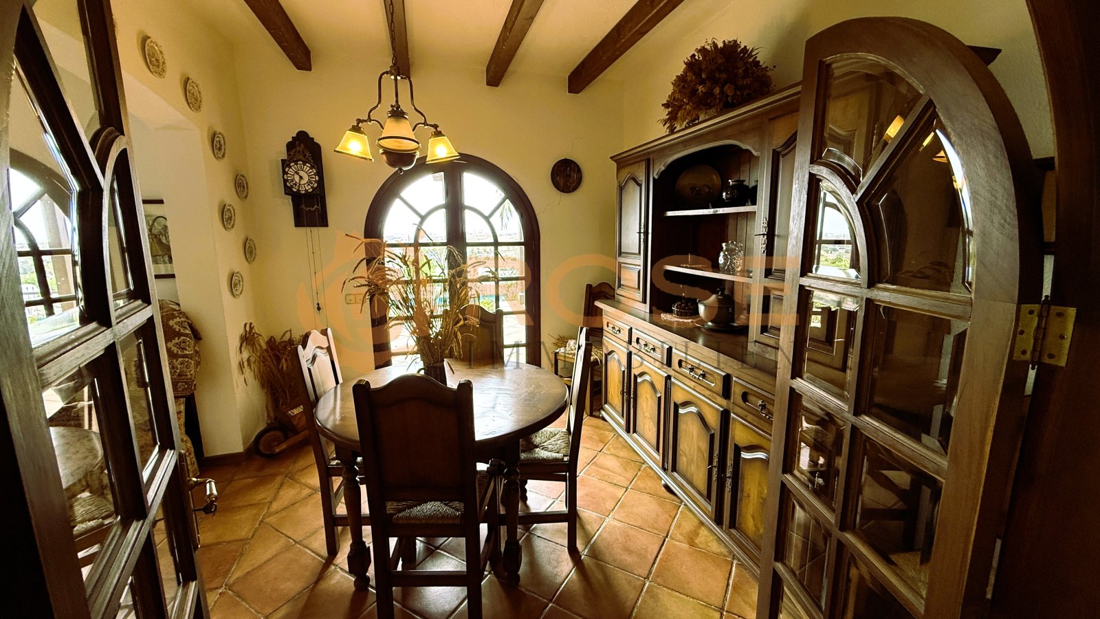 Salle à manger avec poutres en bois apparentes, fenêtres en arc et accès intégré à la cave à vin