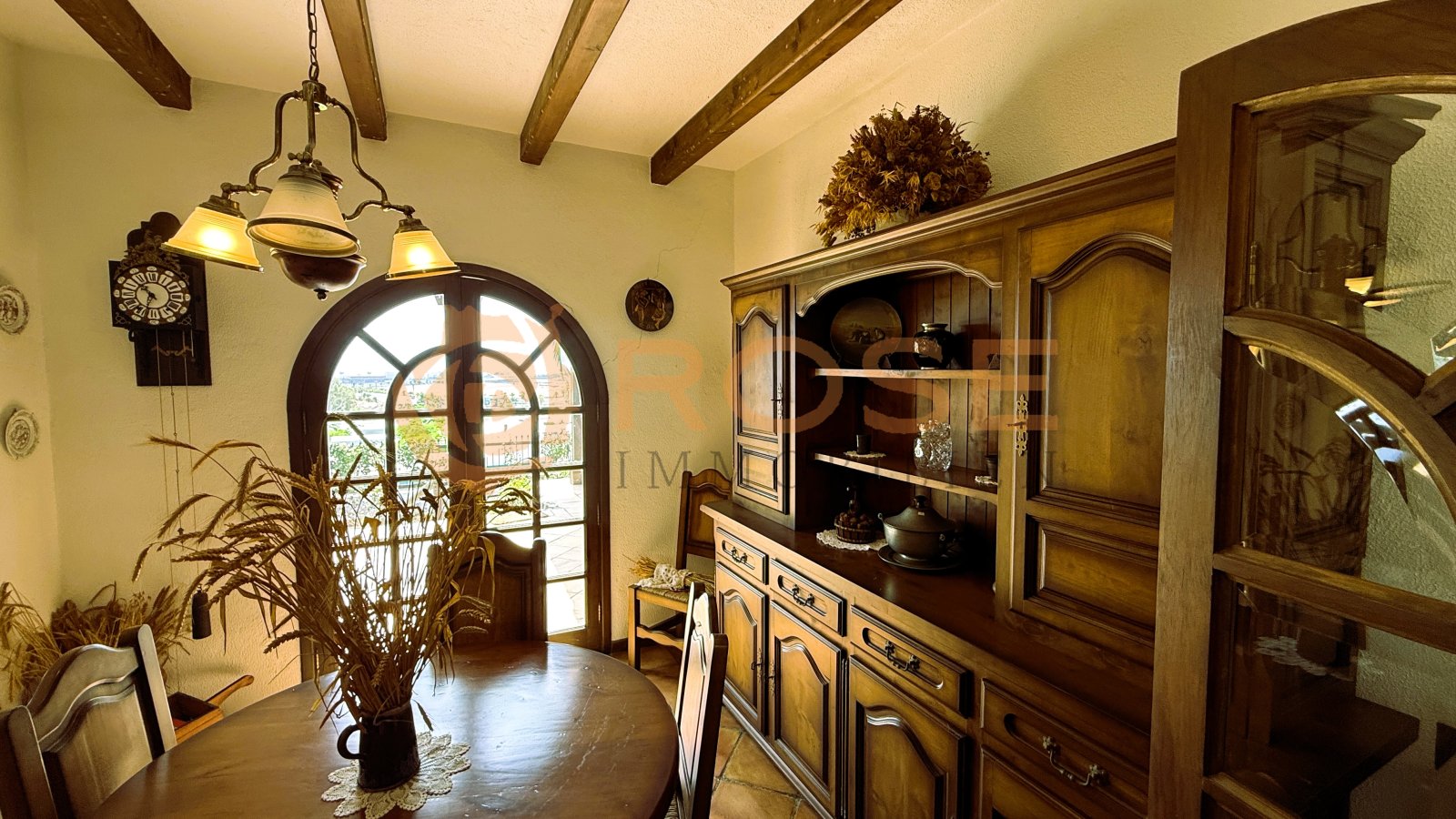Salle à manger avec fenêtres en arc, plafond à poutres en bois et accès direct à la cave à vin